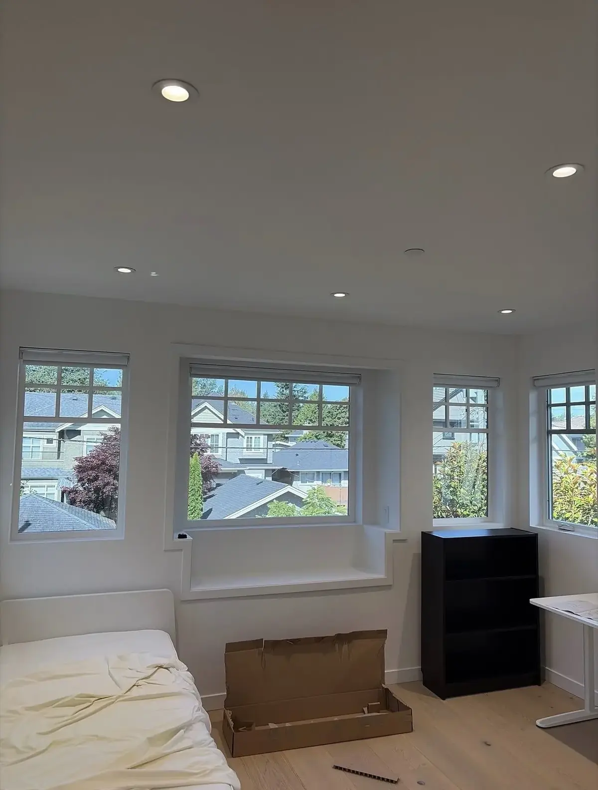 Bedroom with recessed ceiling lights, a bay of windows looking over neighbouring houses, a mattress and a bookshelf