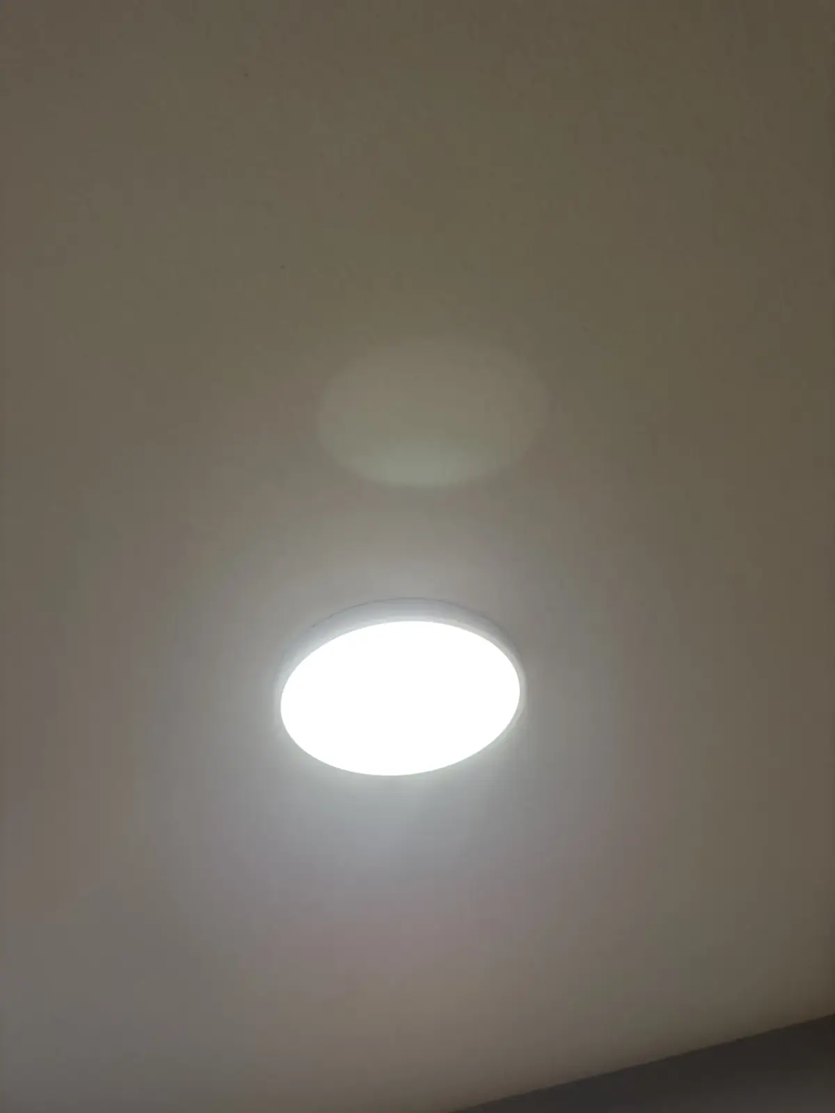 Close view of a round flush-mounted LED ceiling light, switched on, against a white ceiling