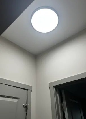 Round flush-mount LED light on a hallway ceiling near two door frames
