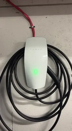 White EV wall connector with a green status light and the charging cable looped around it