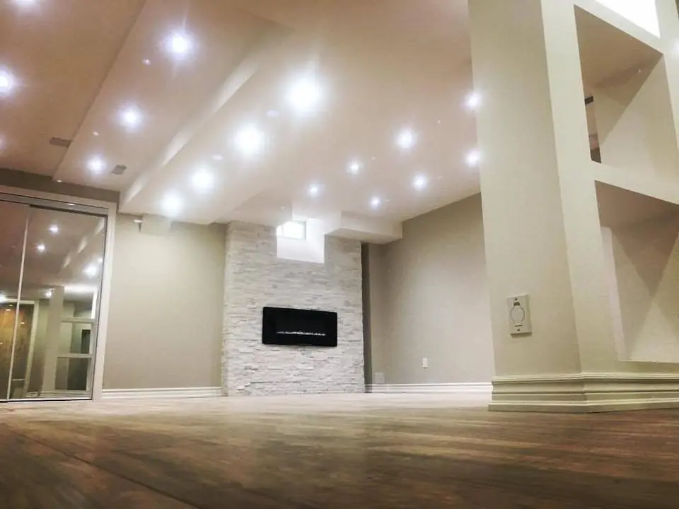 Finished basement with a grid of bright recessed lights and a stone fireplace wall with a linear electric fireplace