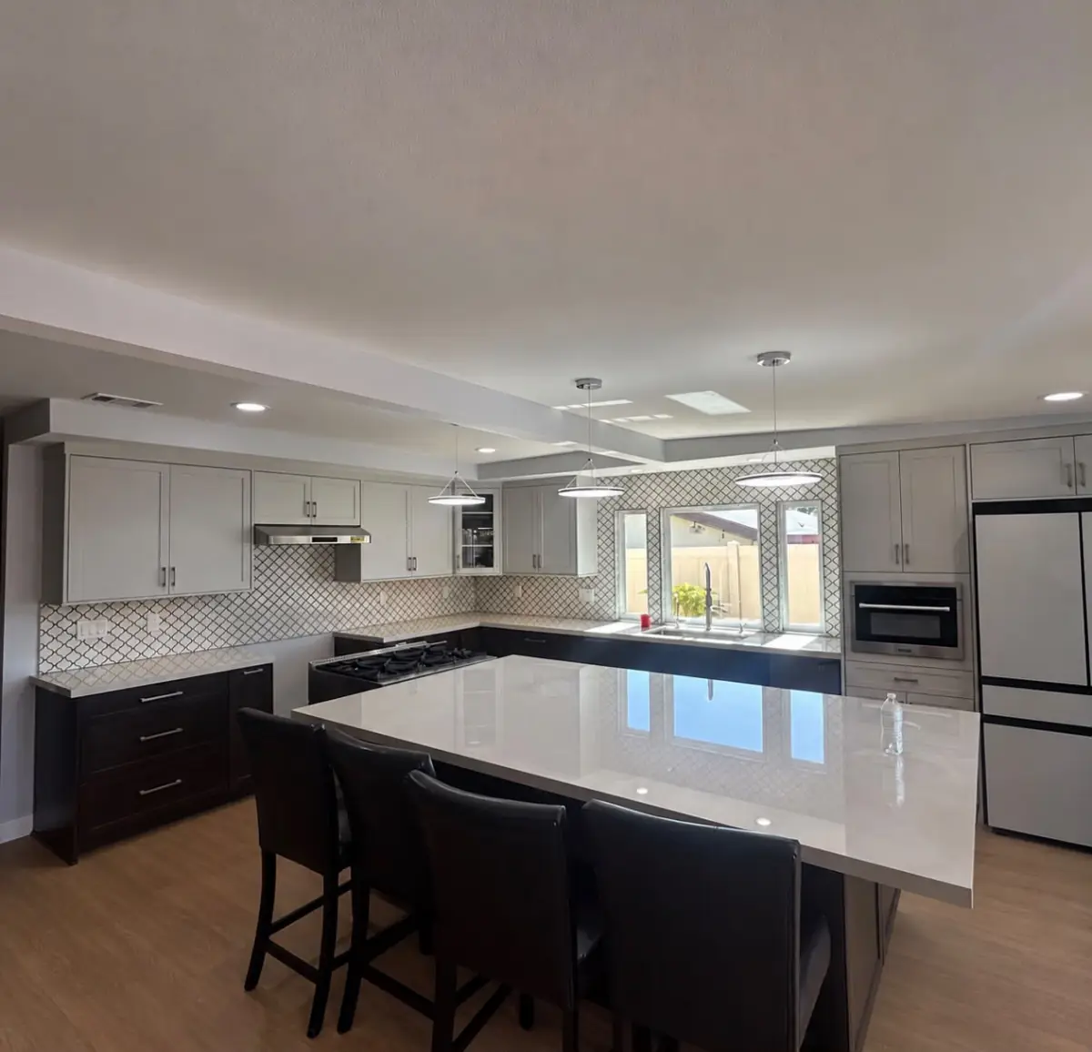 Modern kitchen with three pendant lights over a large island and recessed lights in a dropped ceiling